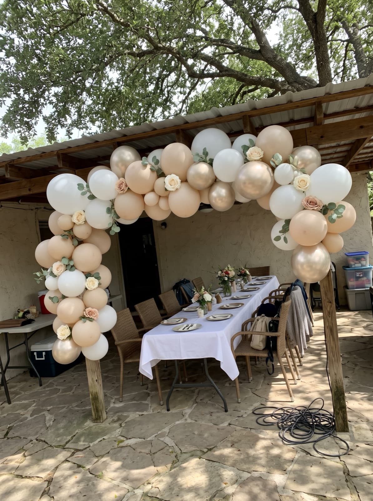 Floral balloon arch with greenery over a brunch table on a shaded stone patio