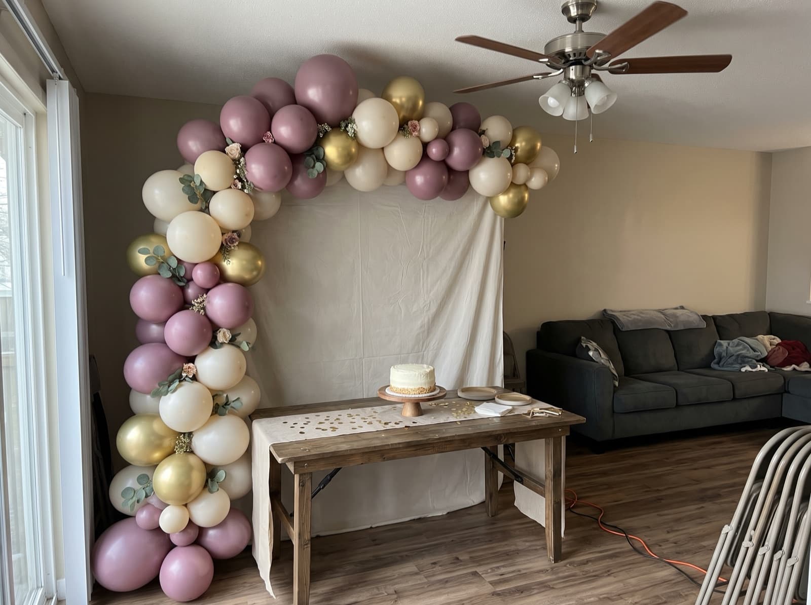 Half balloon arch in mauve, cream and gold swooping over a cake table